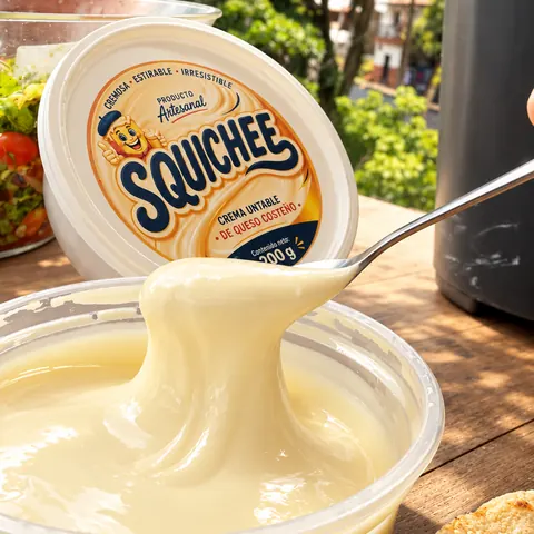 Squichee de 200 g: crema fluida de queso coste&ntilde;o en su pote abierto, con tapa de marca y cuchara